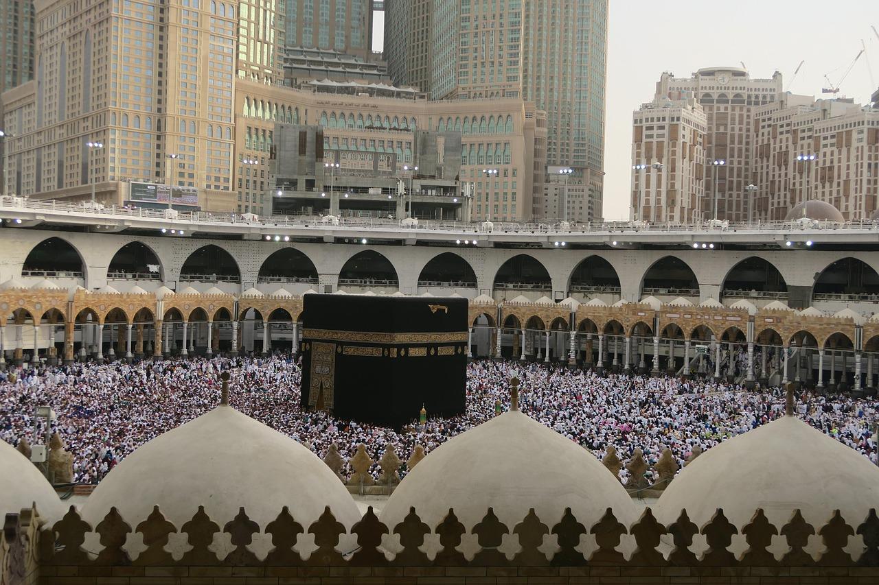 Pilgrims walking together during Hajj surrounded by grand architecture under open skies