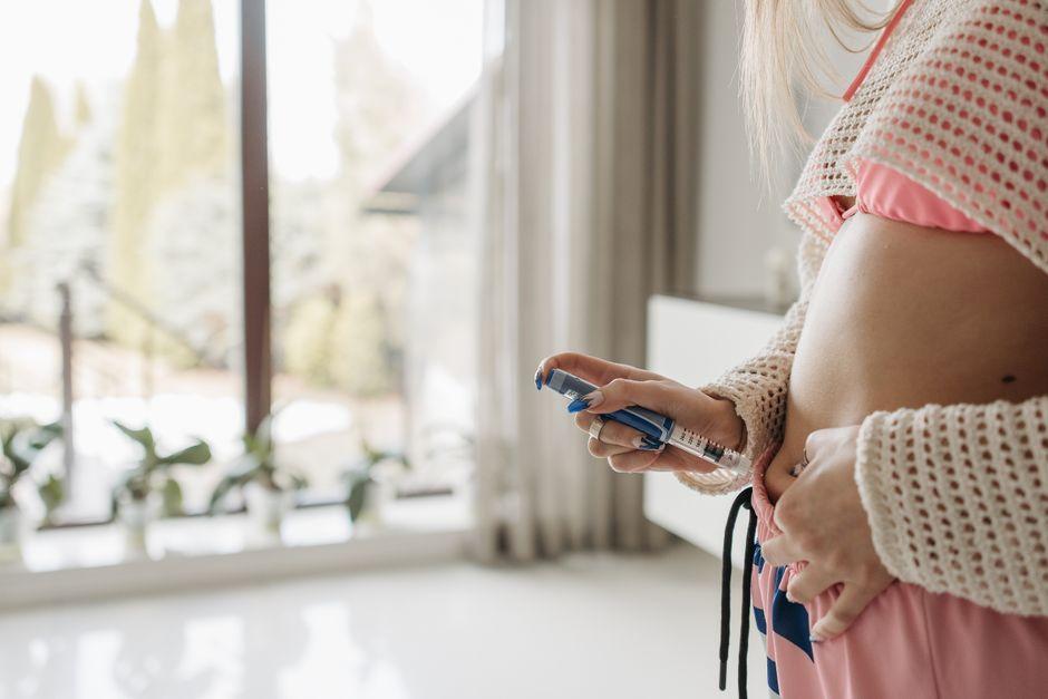 Person holding an insulin pen with a notepad displaying insulin dose timing