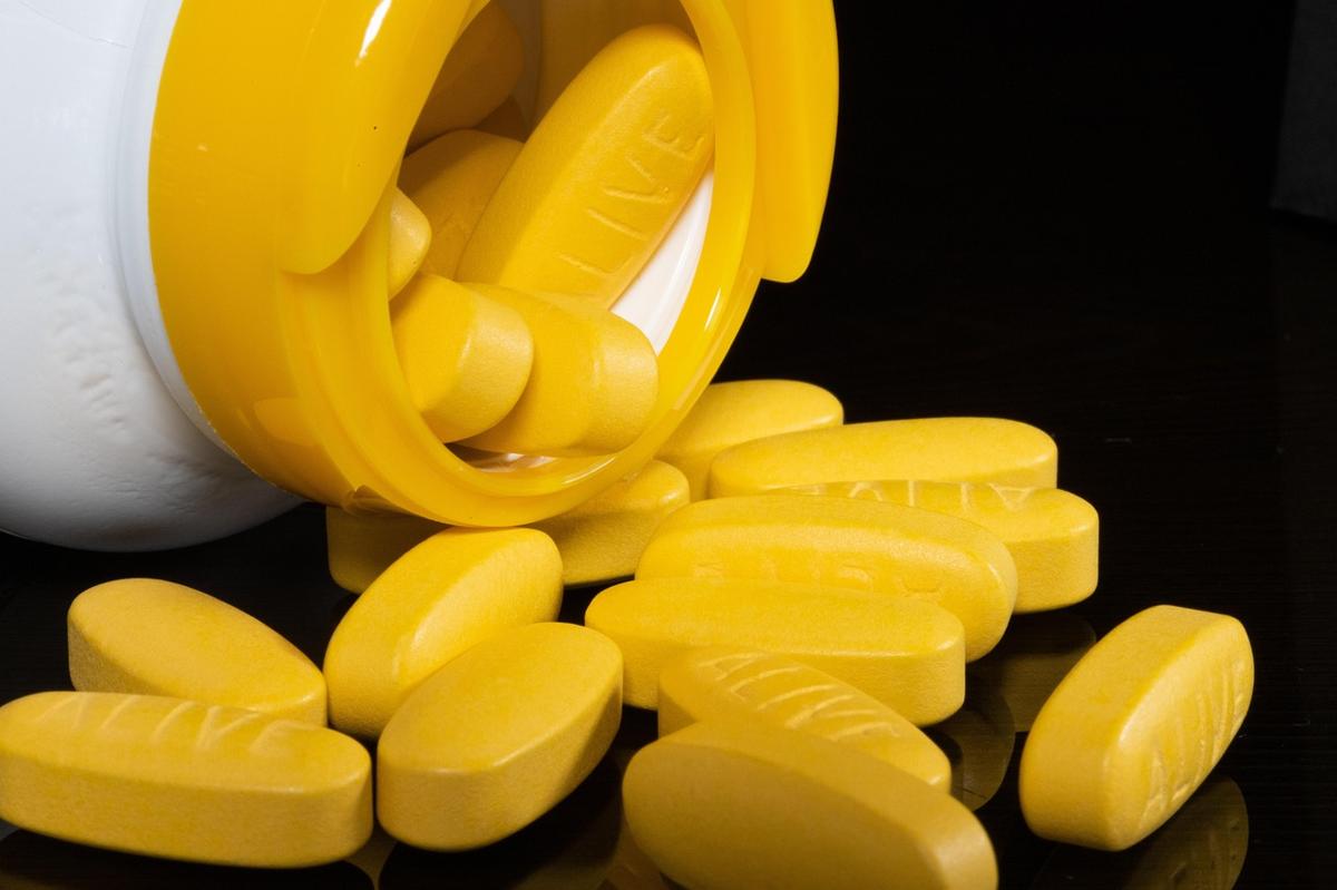 A prescription pill bottle and pharmaceutical tablets sitting beside a wooden mortar and pestle